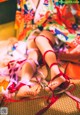 A woman in a colorful kimono sitting on the floor with her feet tied up.