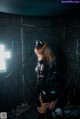 A woman in a black latex outfit standing in a dark room.
