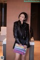 A woman in a black leather jacket leaning against a wall.