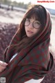 A woman wearing glasses and a plaid blanket on a beach.