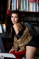 A woman sitting on a red chair in front of a bookshelf.