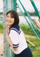 A woman in a school uniform leaning against a fence.