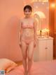 A woman in a pink bikini standing on a bed.