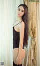 A woman in a black bodysuit leaning against a curtain.